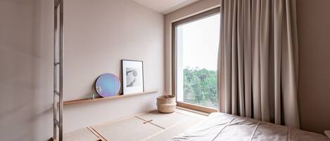Une chambre à coucher au style minimaliste, avec un lit, une fenêtre avec des rideaux, une étagère avec des photos encadrées et une petite table en bois.