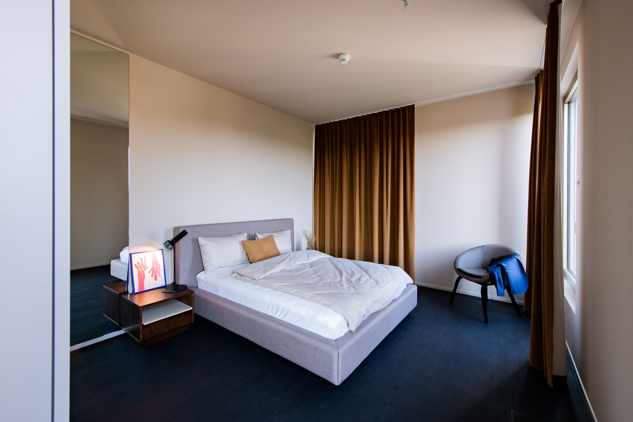 Une chambre d’hôtel moderne avec un grand lit, une table de chevet avec une lampe, une chaise et une fenêtre avec des rideaux.