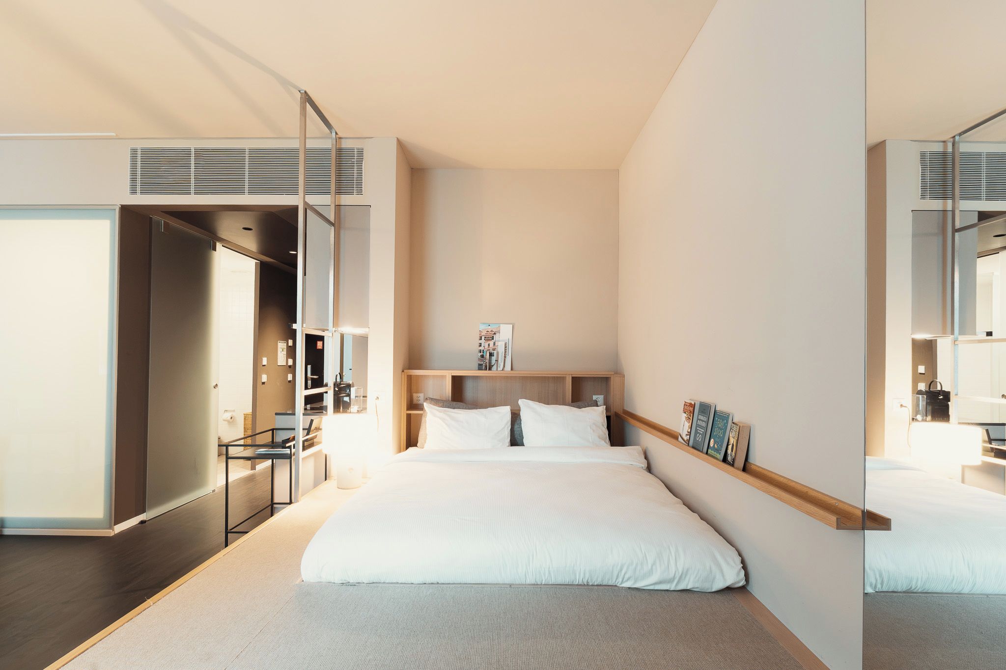 A modern hotel room with a bed, bedside table, and a mirror.