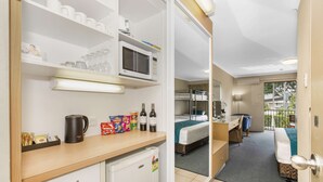 Een compacte hotelkamer met kitchenette, bed, klein bureau en balkon met uitzicht.