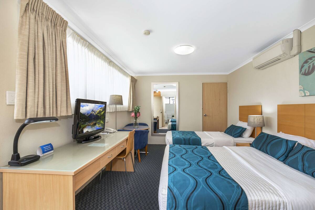 Een hotelkamer met twee bedden, een bureau met een computer, een stoel en een bureaulamp.