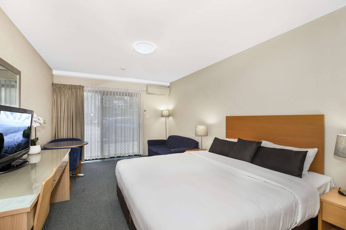 Een hotelkamer met een groot bed, een bureau met een televisie, een stoel en een raam met gordijnen.