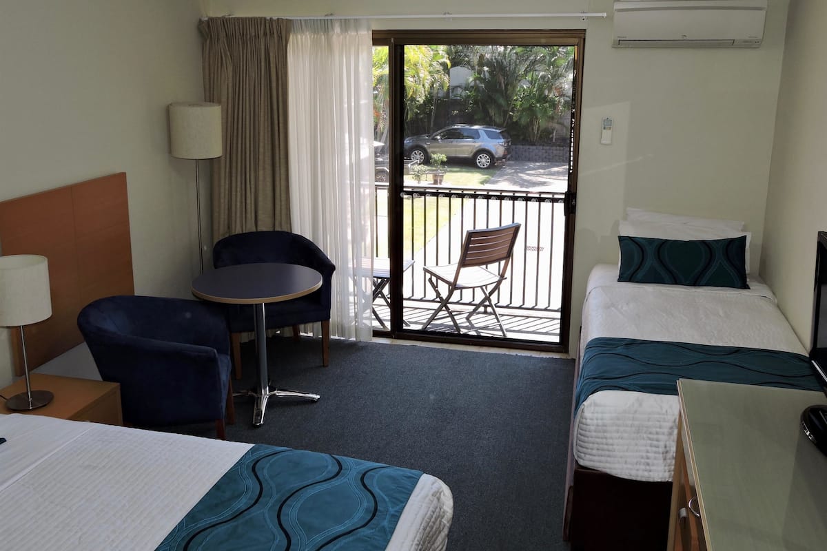 Hotelkamer met twee enkele bedden, een klein tafeltje met een stoel, een lamp en uitzicht buiten door een schuifdeur.