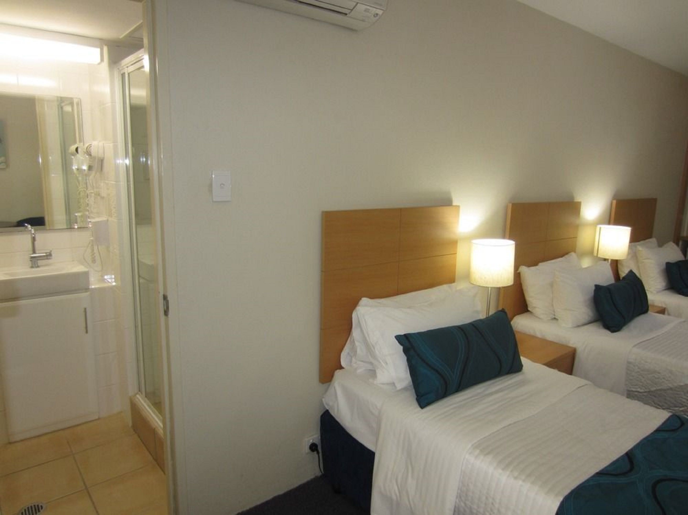 Habitación de hotel con dos camas, baño con lavamanos y espejo.