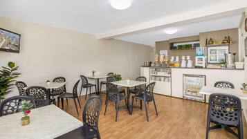 Un espace repas comprenant plusieurs tables et chaises, un réfrigérateur et un comptoir où sont disposés divers objets.