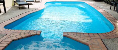 A rectangular swimming pool with a brick border and a hot tub area.