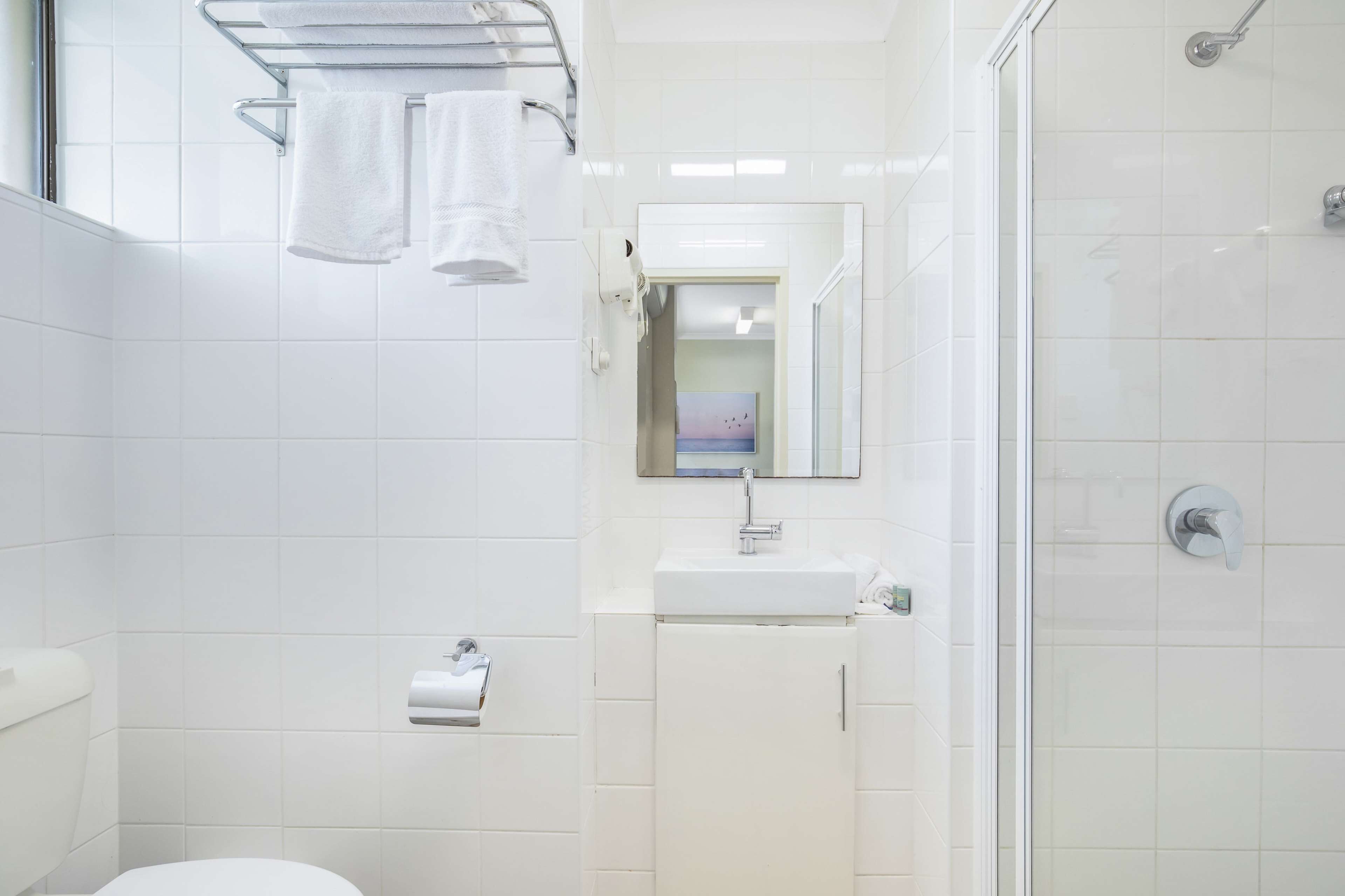 Een moderne badkamer met witte tegels, een glazen douchecabine, een wit wastafelmeubel en een handdoekrek.