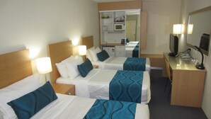 Een hotelkamer met drie éénpersoonsbedden, een bureau met een computer, een spiegel en een kleine kitchenette.