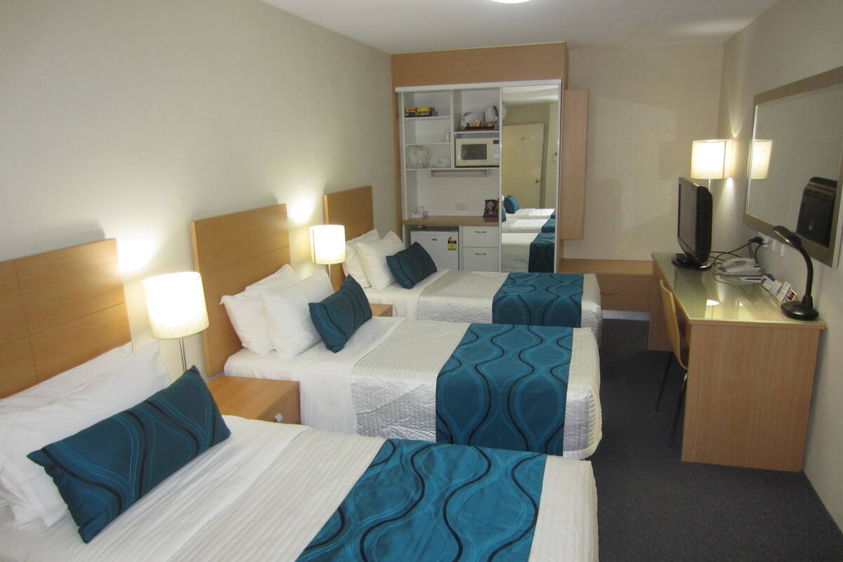 Een hotelkamer met drie éénpersoonsbedden, een bureau met een computer, een spiegel en een kleine kitchenette.