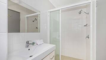 A modern bathroom with a white sink, mirror, and glass-enclosed shower.