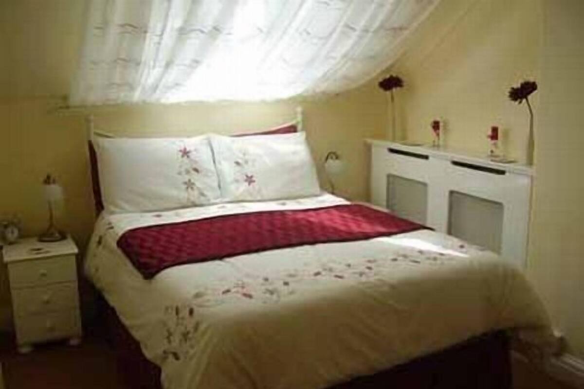 A bedroom with a bed, nightstand, dresser, and a window with curtains.