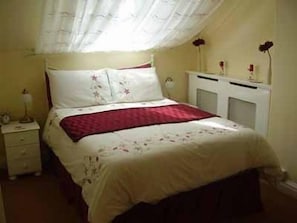 A bedroom with a bed, nightstand, dresser, and a window with curtains. - Aidansdale Hotel (Bridlington)
