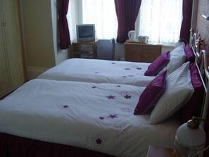 A hotel room with two beds, each with white bedding and purple accents, a small television on a wooden stand, and a window with curtains. - Aidansdale Hotel (Bridlington)
