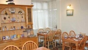 A dining area with wooden tables and chairs, a wooden cabinet with decorative items, and a wall-mounted light fixture.