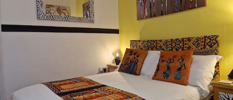 A bed with a patterned bedspread, a zebra-striped mirror, and a wall with a colorful painting.
