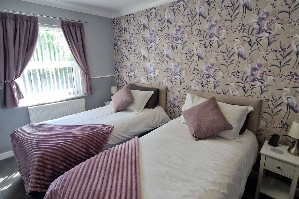 A room with two beds, a ceiling fan, and a window with curtains.