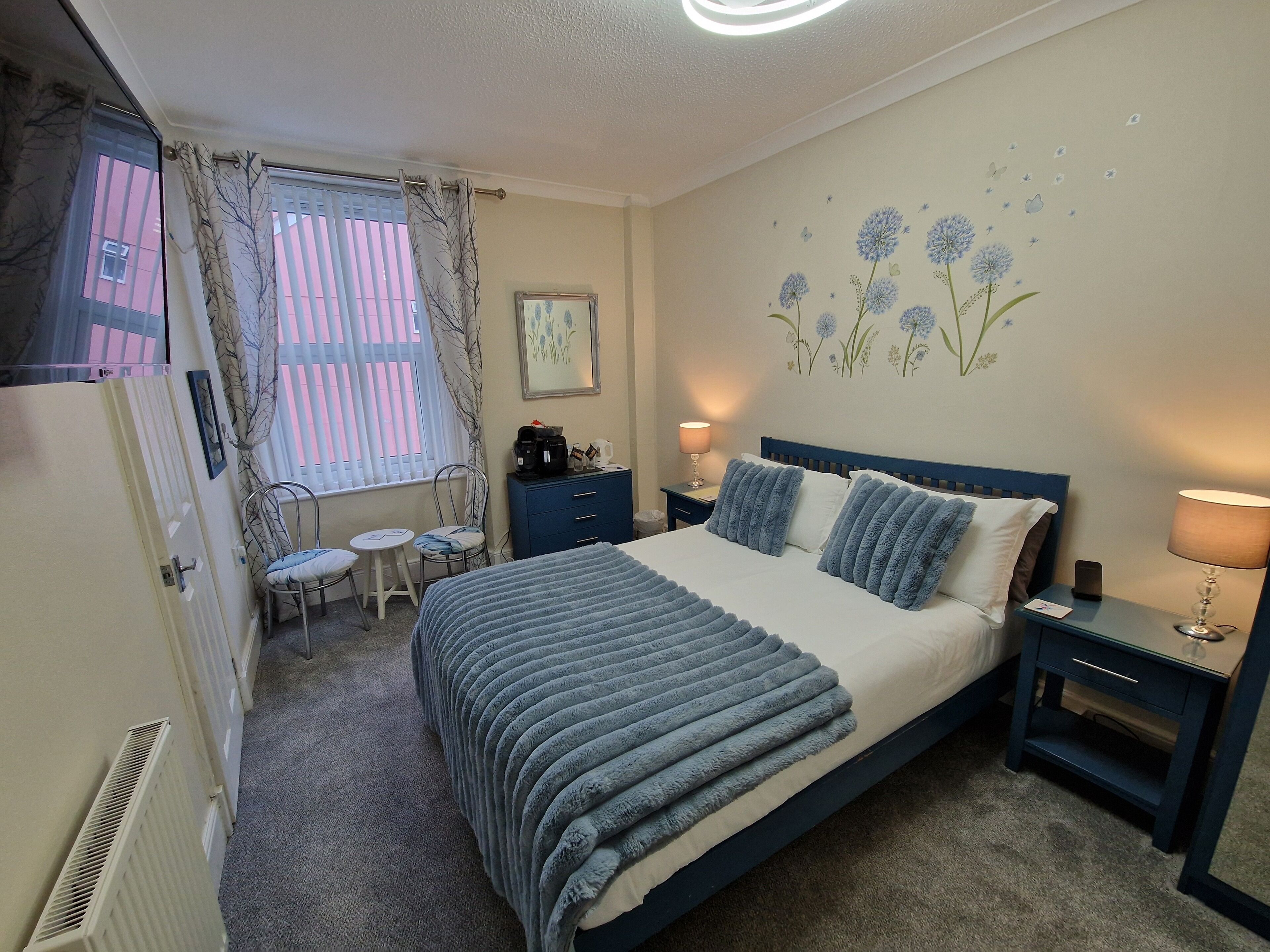 A bedroom with a bed, bedside tables, a desk, a chair, and a window with curtains.