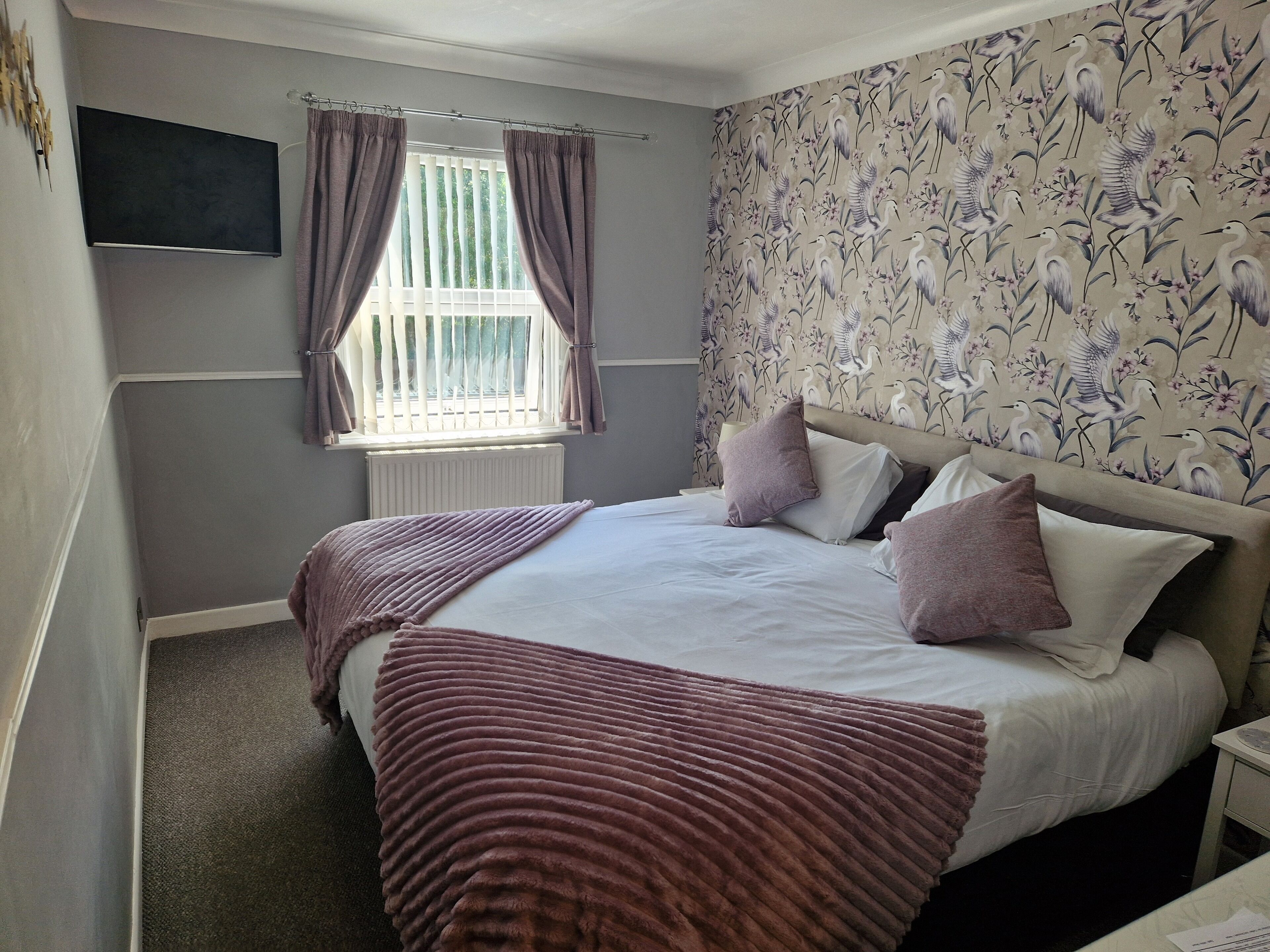 A bedroom with a bed, curtains, a window, and a wall with a floral pattern.