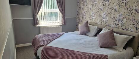 A bedroom with a bed, curtains, a window, and a wall with a floral pattern.