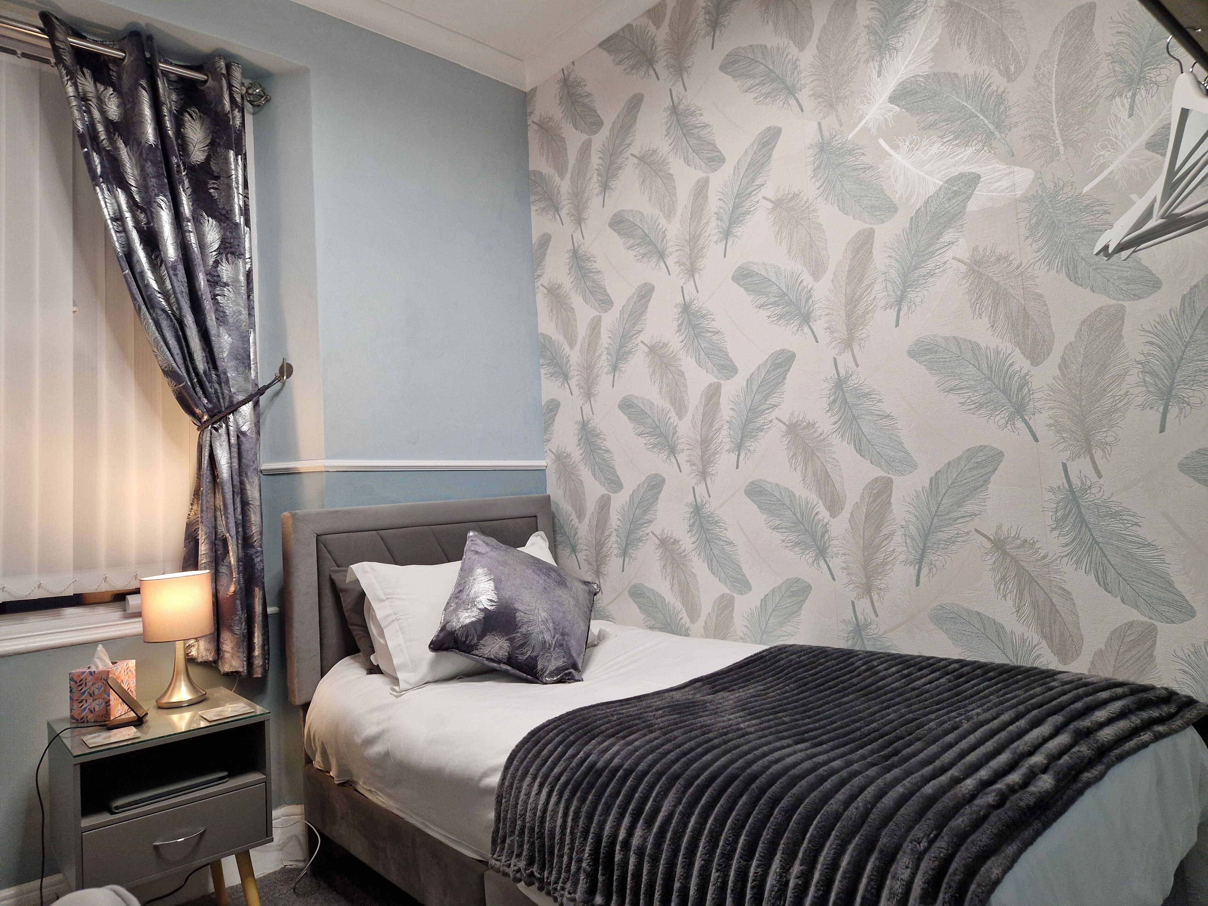 A bedroom with a bed, nightstand, lamp, and a feather-patterned wall.