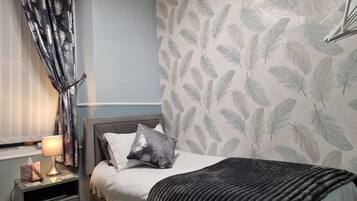 A bedroom with a bed, nightstand, lamp, and a feather-patterned wall.