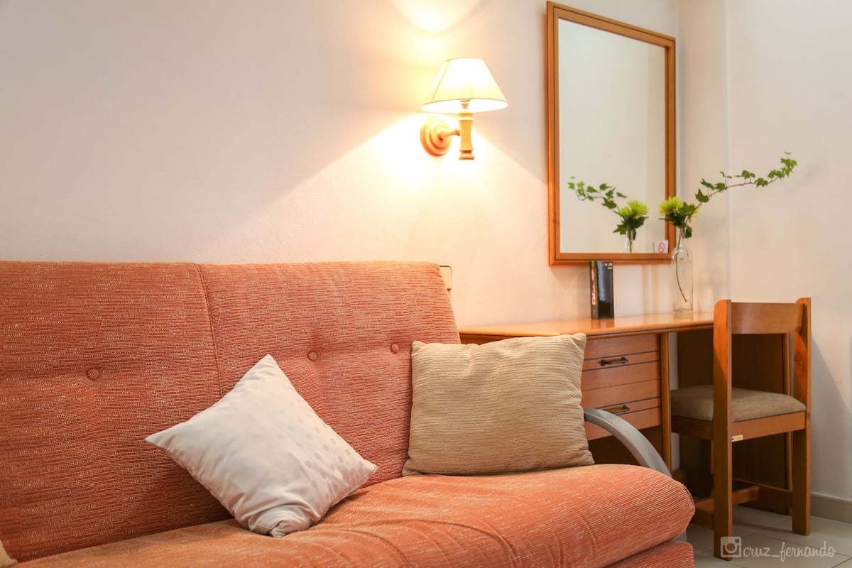 Ein Zimmer mit einer Couch, einem Holztisch, einer Lampe und einem Spiegel.