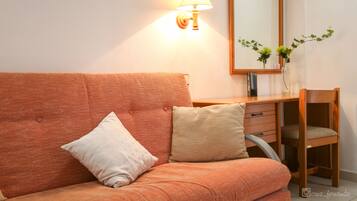 A room with a sofa, a wooden desk, a lamp, a mirror, and a vase with plants.