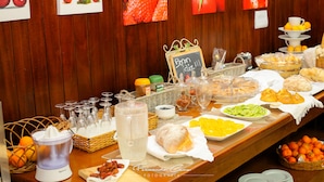 A buffet table with various food items and beverages, including fruits, pastries, and a juice dispenser.