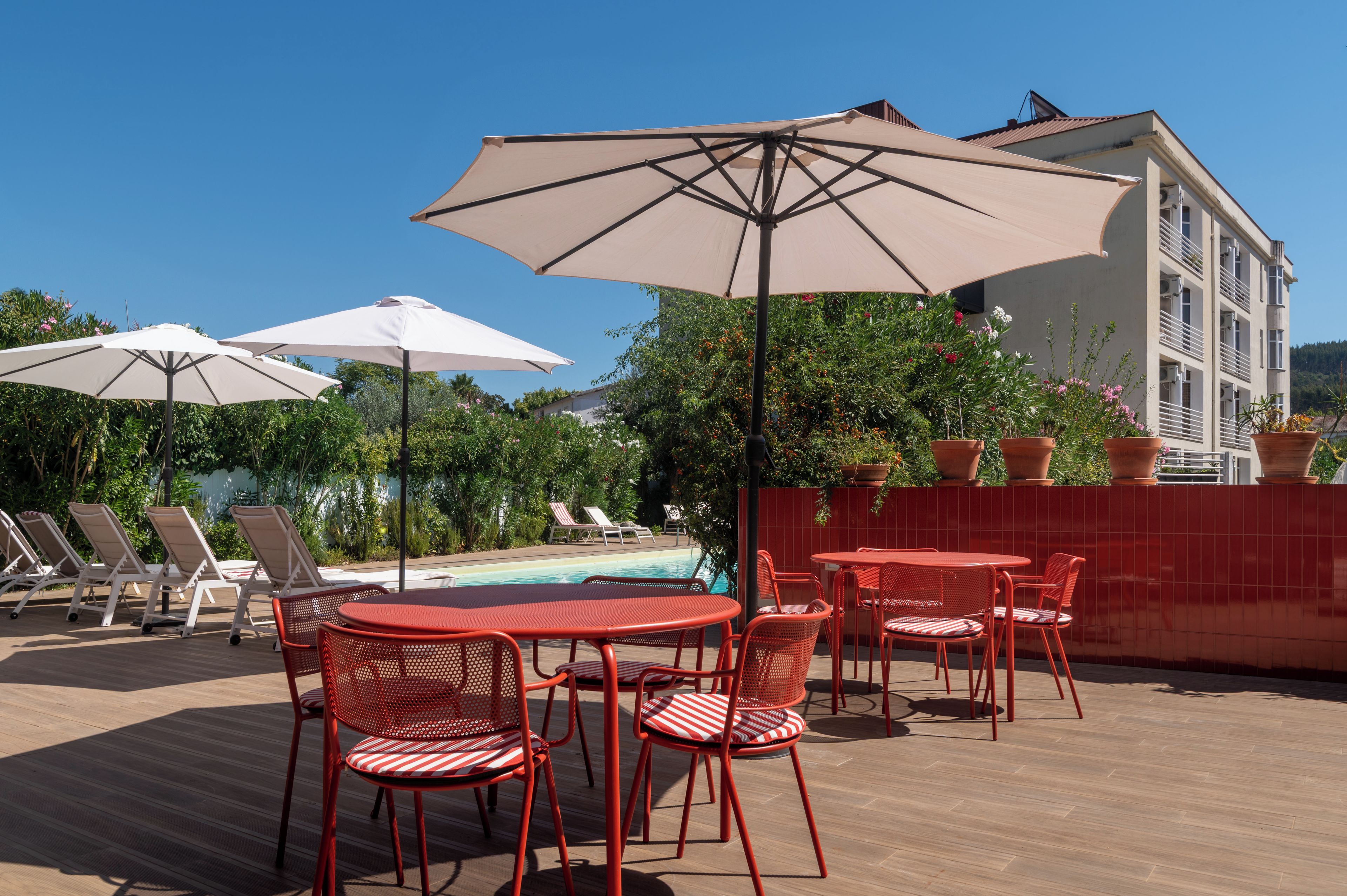 Ein Poolbereich auf dem Dach mit Liegestühlen, roten und weißen Streifenstühlen und Sonnenschirmen.