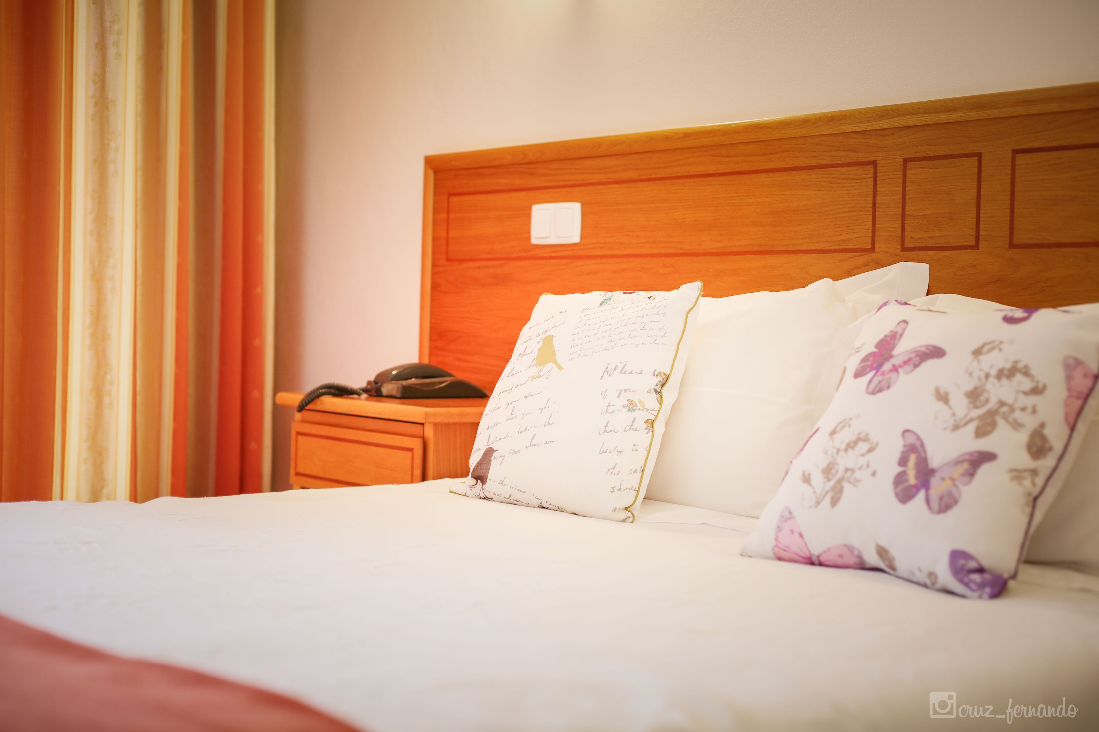 Un letto rifatto con cuscini floreali, una testiera in legno e un comodino con il telefono.