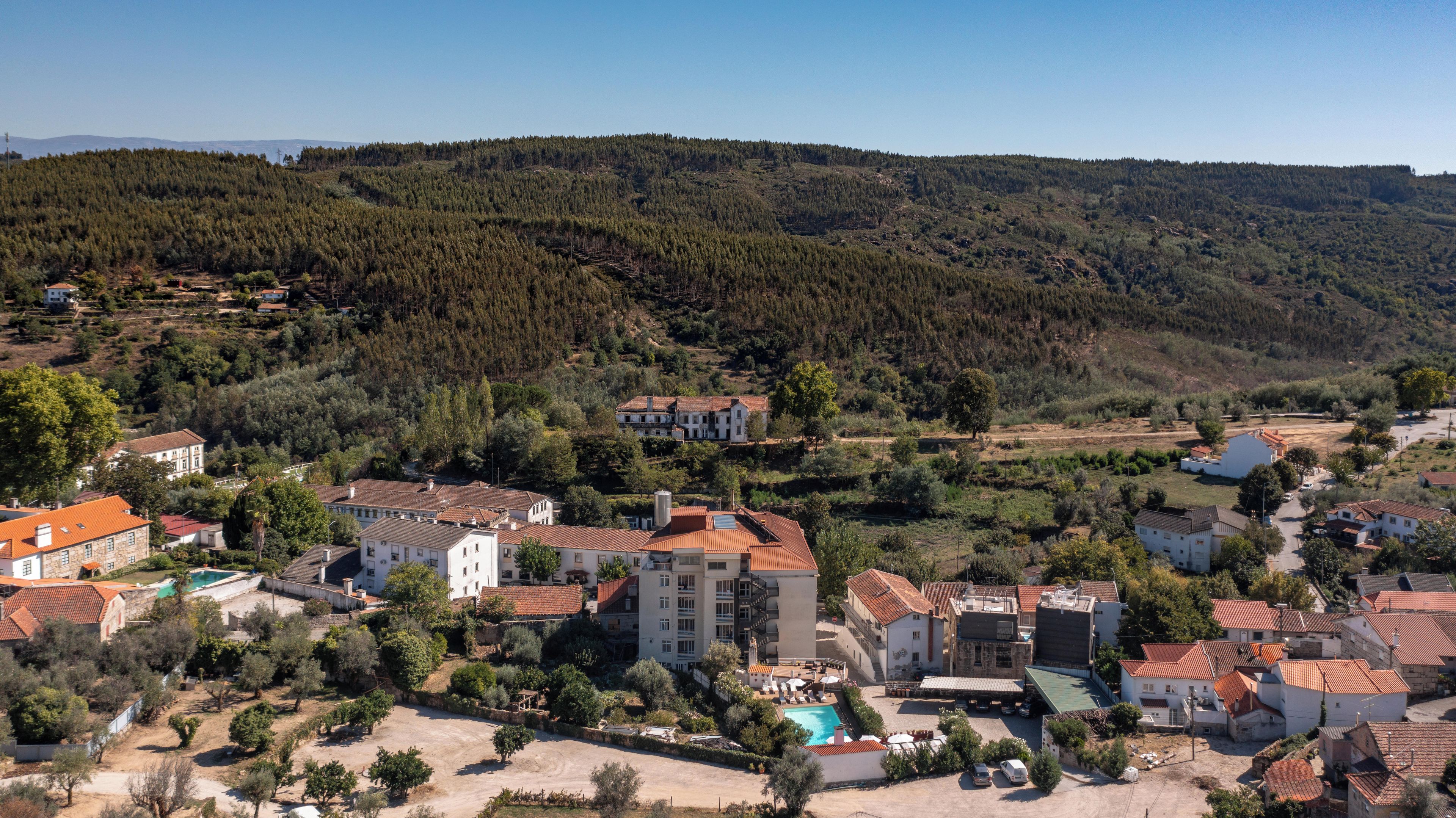 A residential area with houses, a swimming pool, and a hilly forested background.
