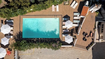 An aerial view of a rooftop pool area with a clear blue pool, surrounded by lounge chairs and umbrellas.