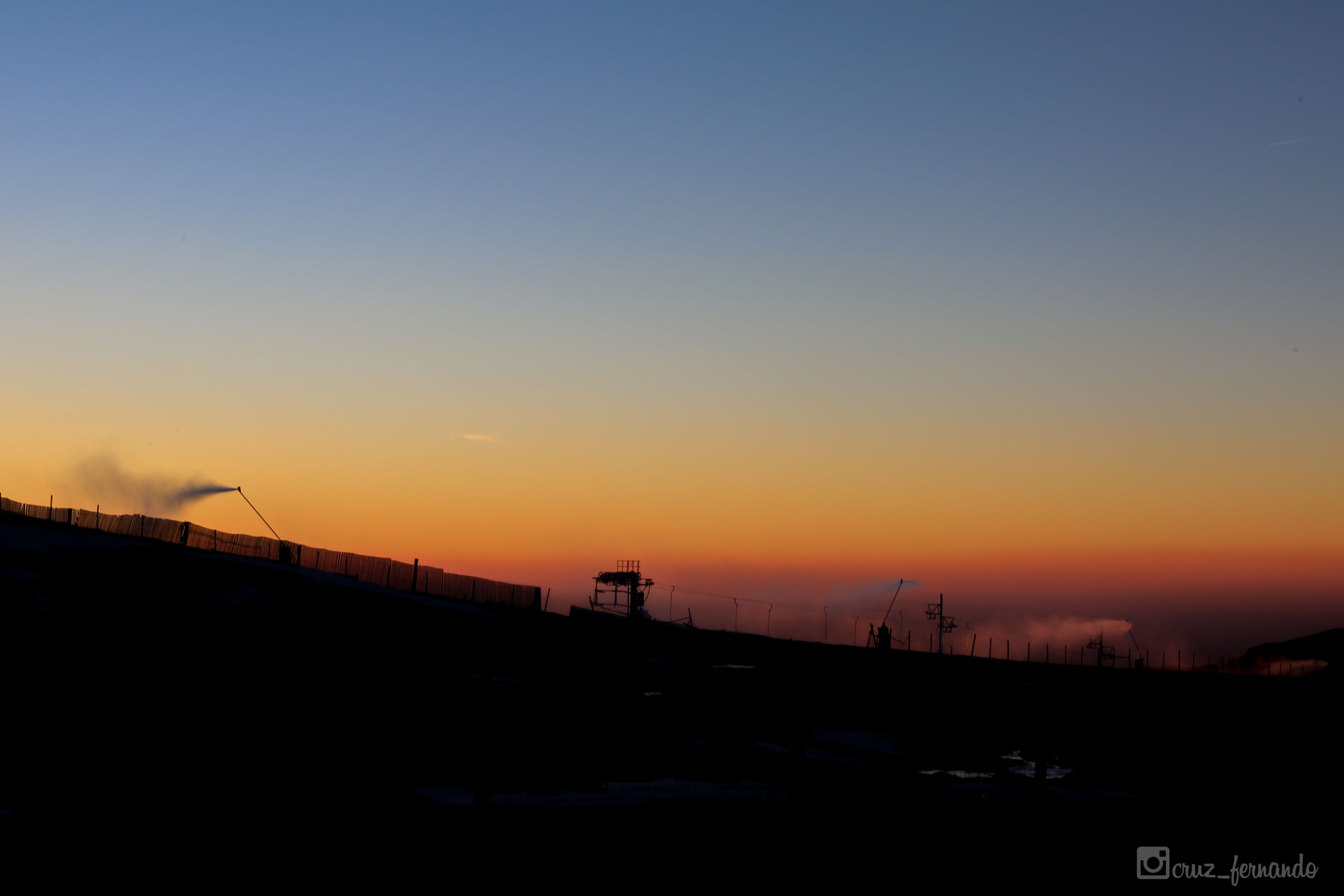 A silhouette of a fenced area with a structure in the middle, possibly a control tower or observation post, during sunset or sunrise.
