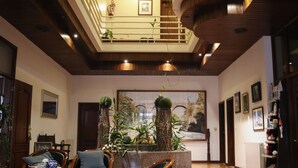 A spacious lobby with a high ceiling, wooden flooring, and a central seating area with chairs and a red rug. There are potted plants and a large painting on the wall. -  Hotel Pantanha Nature & Fitness (Nelas)