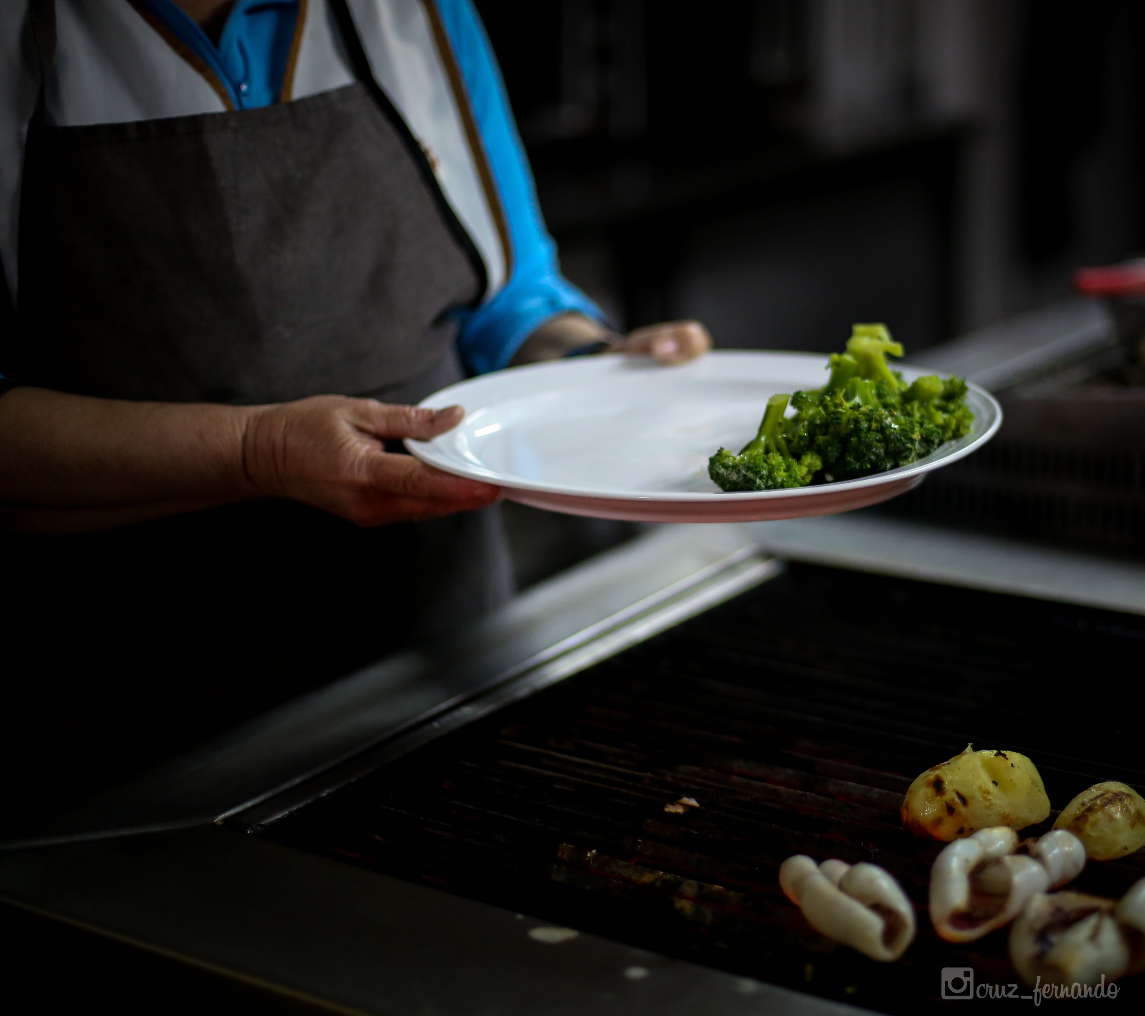 A person holding a plate with broccoli and roasted potatoes.