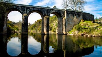 Eine Steinbrücke mit drei Bögen über einem ruhigen Fluss, umgeben von Grünflächen und Bäumen.