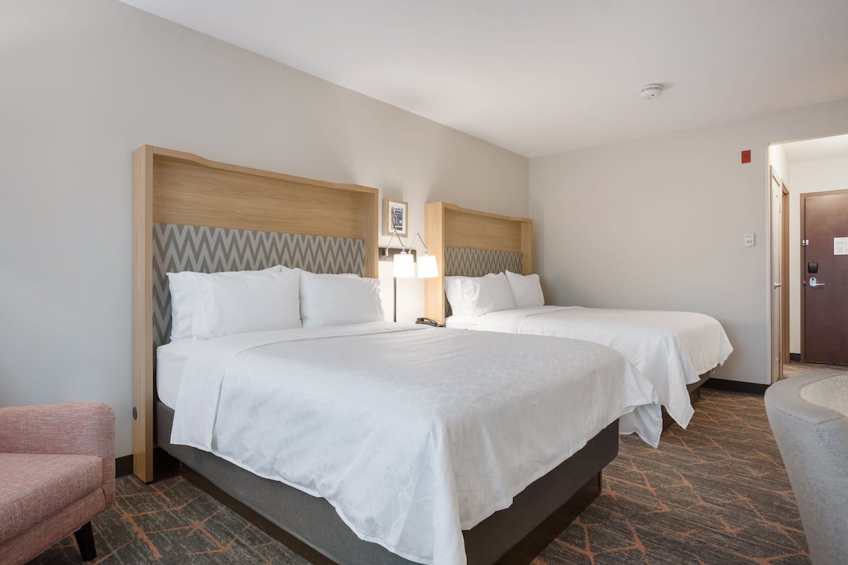 A hotel room with two beds, a desk, a chair, and a lamp.