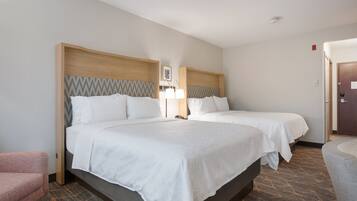 A hotel room with two beds, a desk, a chair, and a lamp.