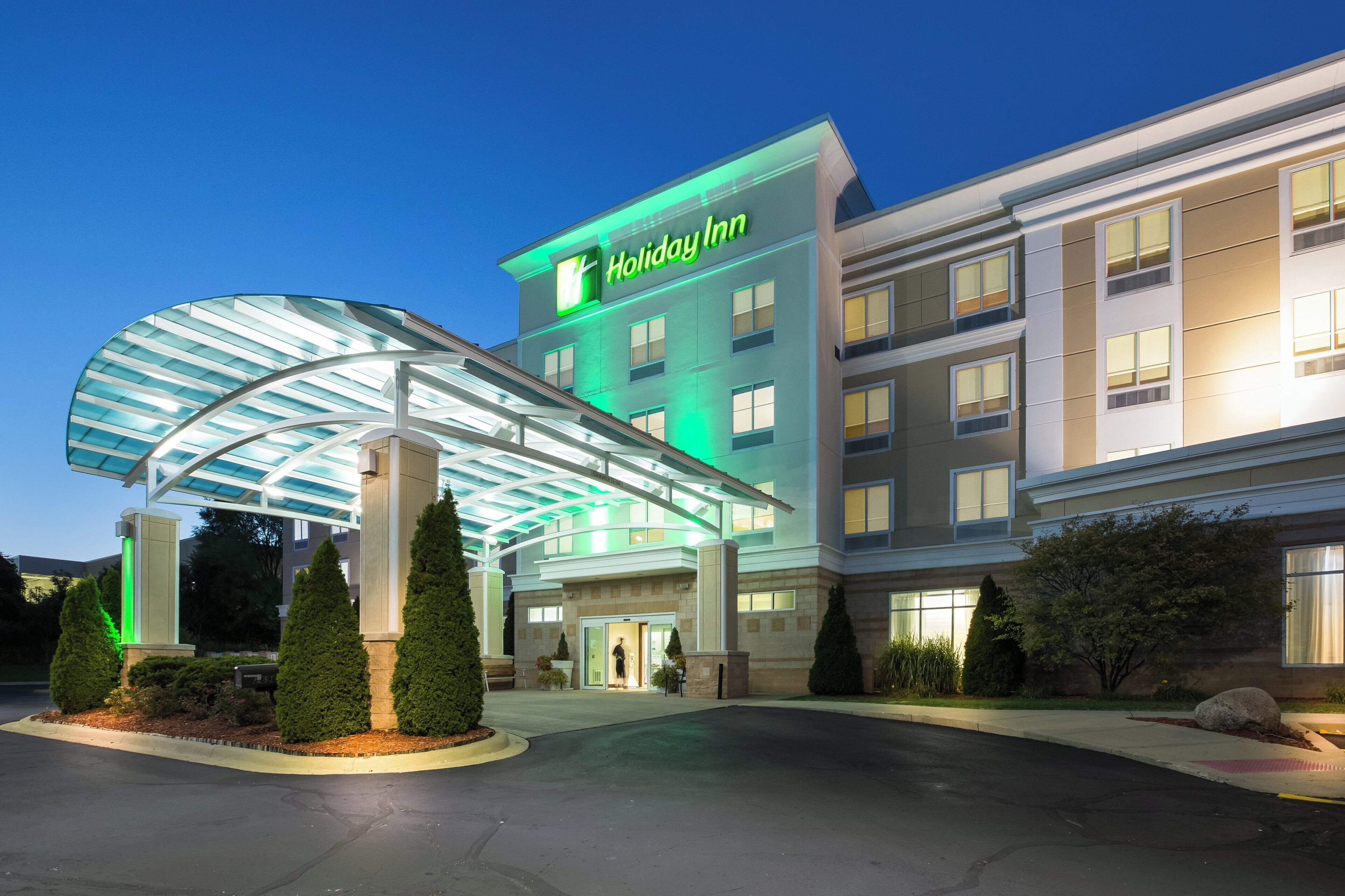 A Holiday Inn hotel with a modern glass entrance canopy, multiple floors, and a well-maintained landscaped area.