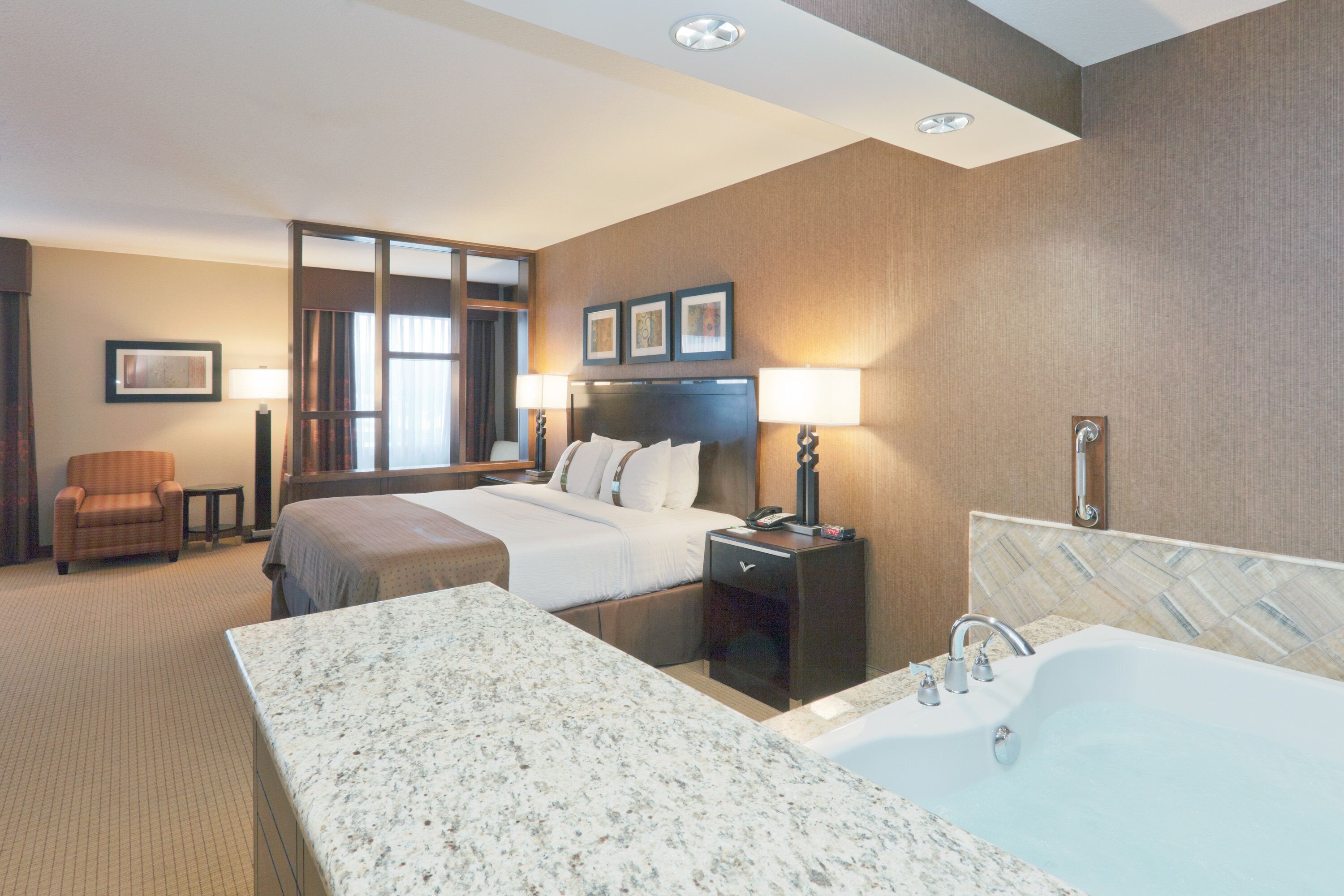 A hotel room with a large bed, a separate sitting area, a bathroom with a bathtub, and a desk with a lamp.