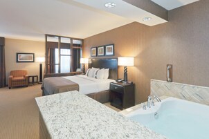 Habitación de hotel con una cama grande, un área de estar separada, un baño con bañera y un escritorio con lámpara.