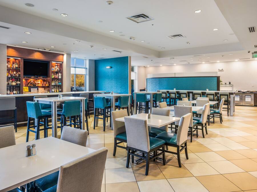 Un restaurante moderno con una zona de bar, diversas opciones de asientos, incluyendo cabinas y mesas, y una pared de acento azul.
