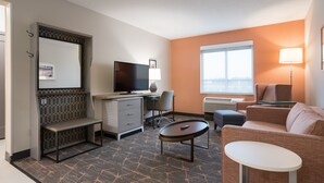 Una habitación de hotel con escritorio, televisor, sofá, mesita y banco.