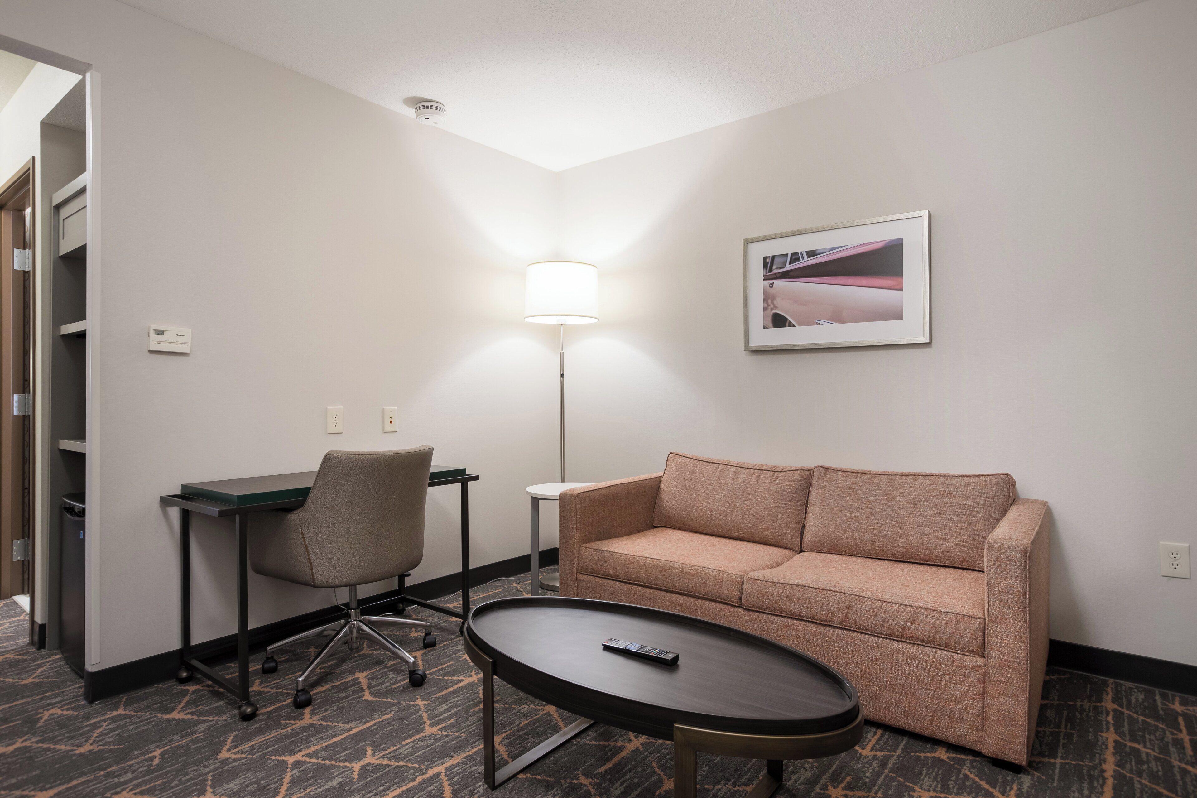 Une chambre d’hôtel équipée d’un bureau, d’une chaise, d’un canapé et d’une petite table sur laquelle se trouve une télécommande.