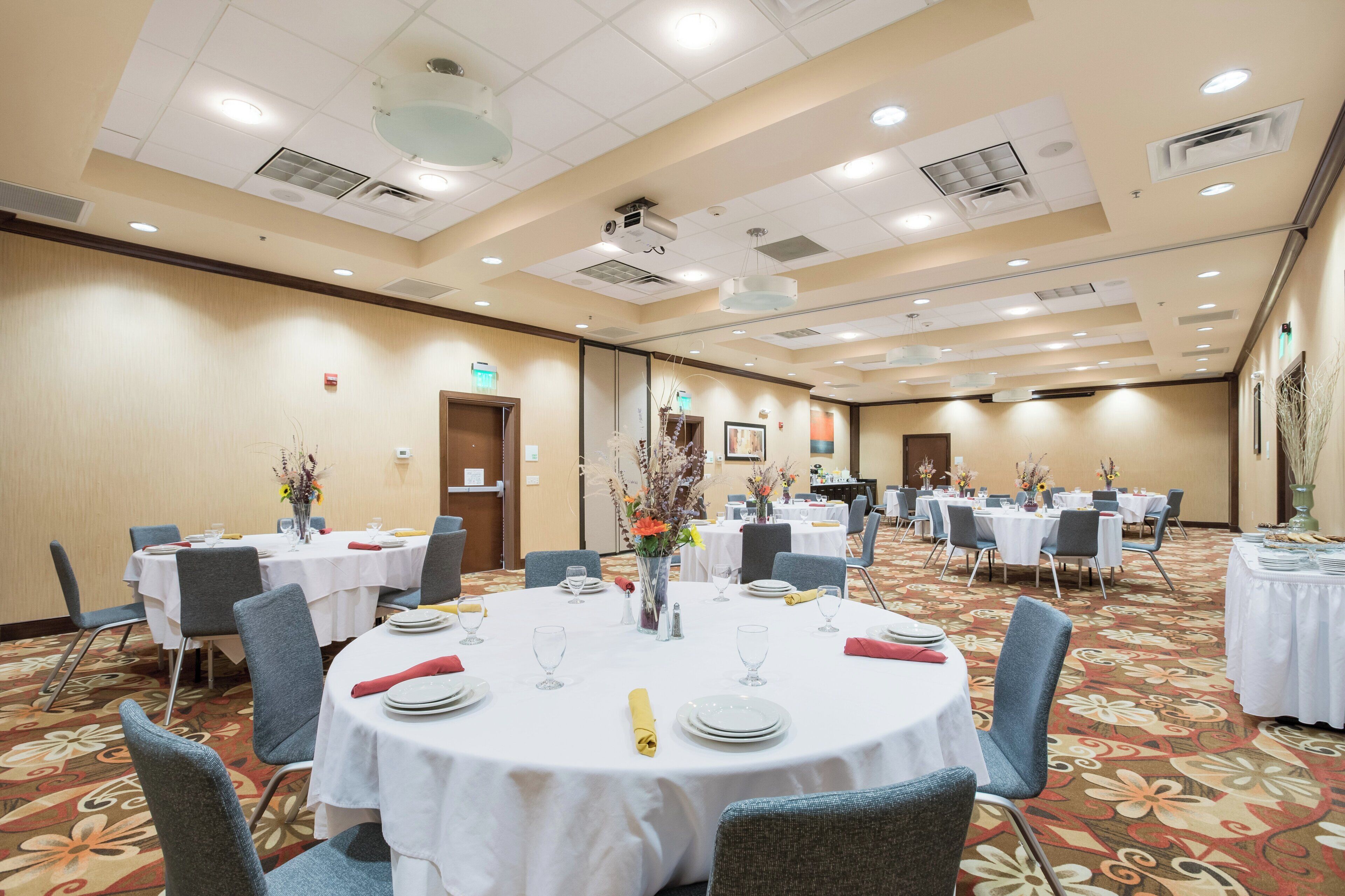 Uma sala de conferências de hotel com mesas redondas, cadeiras e arranjos florais.