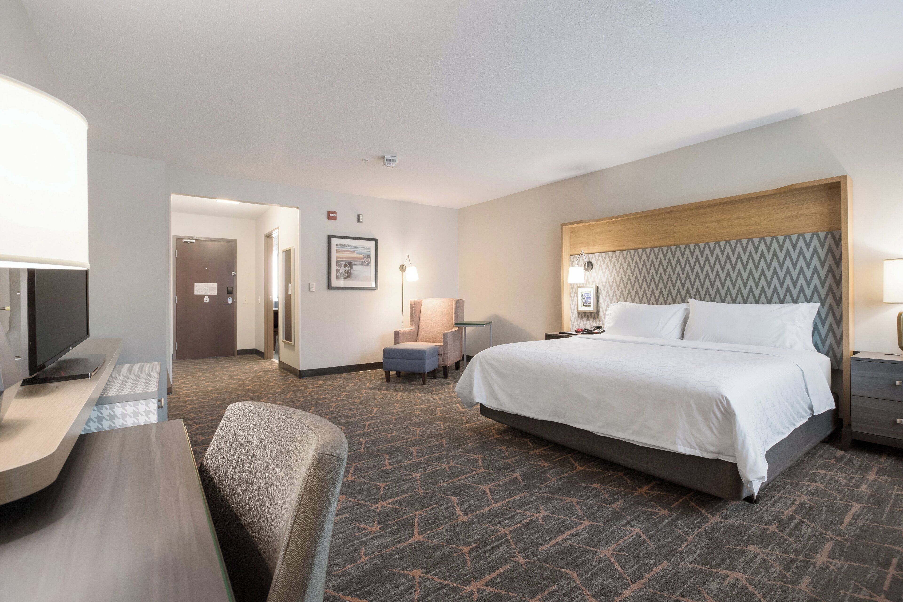 A hotel room with a bed, desk, chair, and a television.