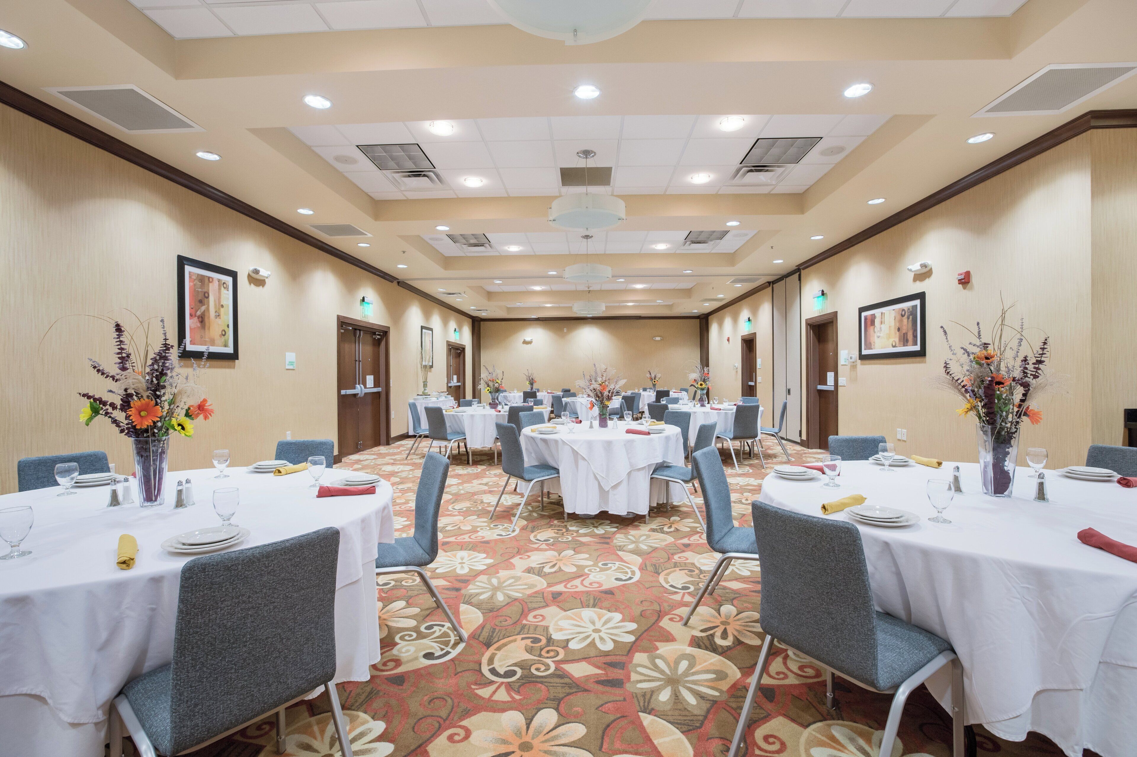 A hotel conference room with multiple tables set for dining, equipped with chairs and table settings.