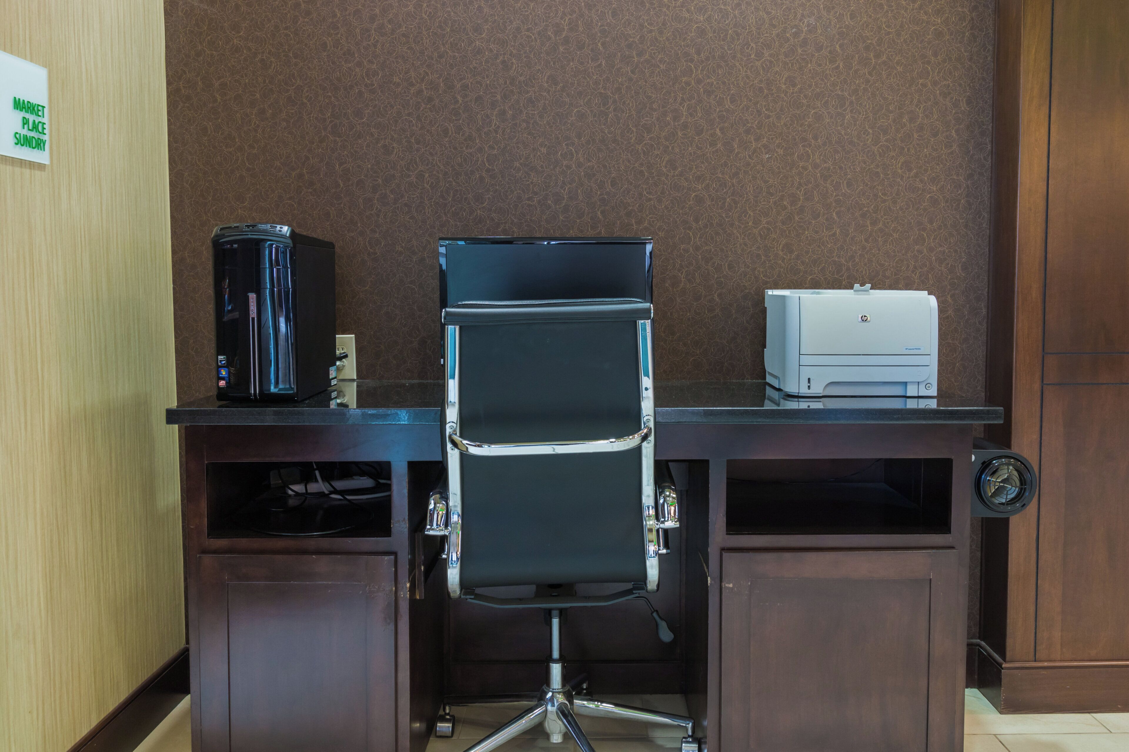 A hotel office with a desk, a black office chair, a coffee machine, and a printer.