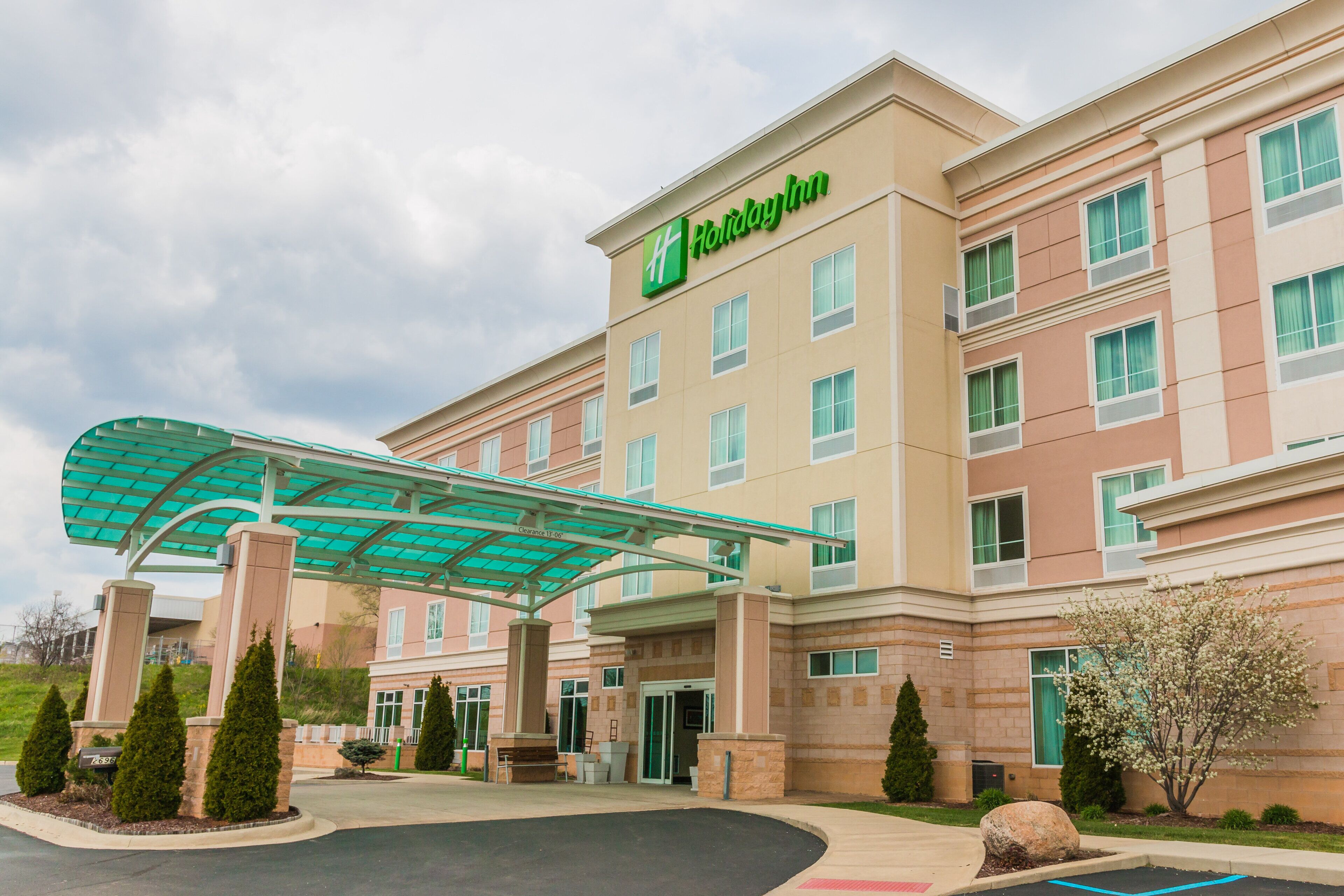 A Holiday Inn hotel with a covered entrance, multiple floors, and a landscaped area with trees and a rock.