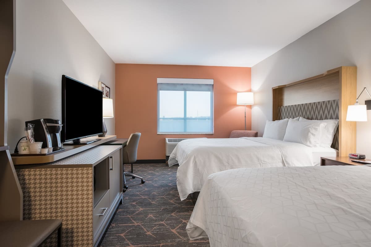 A hotel room with two beds, a TV, a desk, and a window with a view.